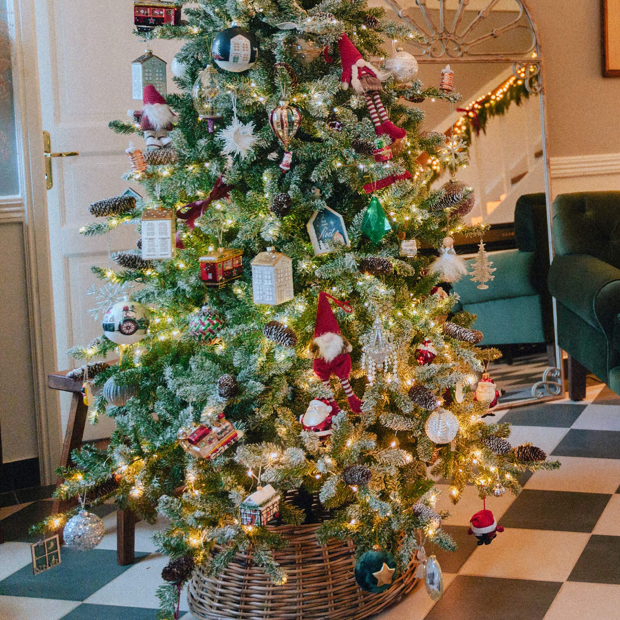 Albero di Natale decorato con luci e ornamenti vari in un cesto di vimini su pavimento a scacchi