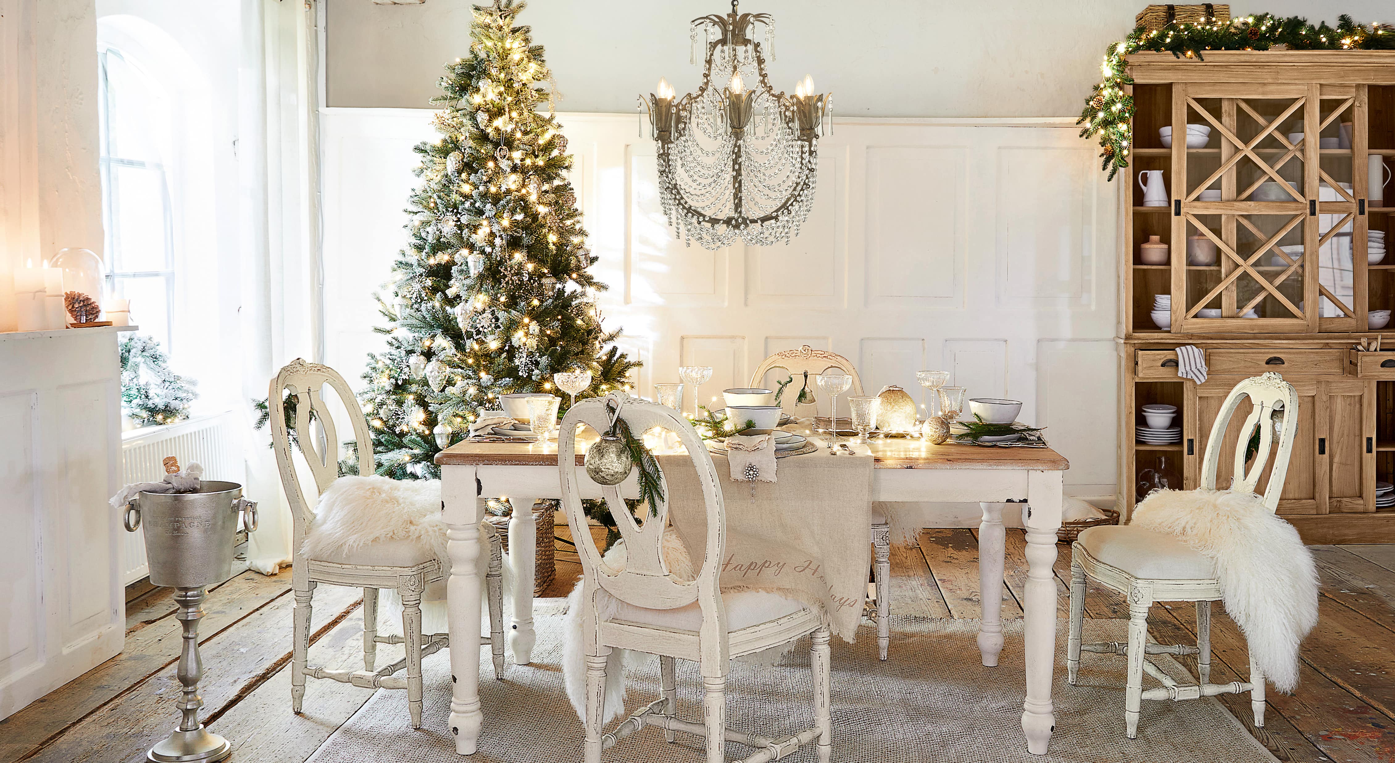 Sala da pranzo con tavolo e sedie bianche in legno, decorata per Natale con albero e lampadario di cristallo