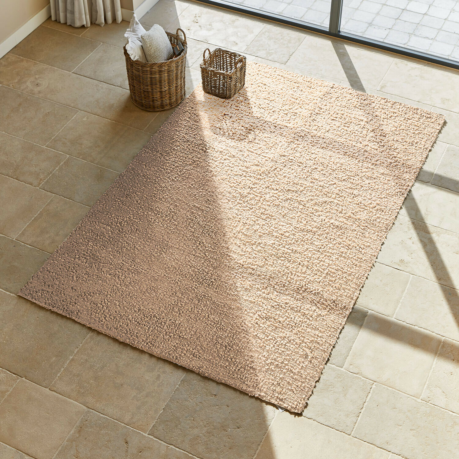 Tappeto Wodaha Tappeto beige in materiale morbido su pavimento in pietra chiara con cesti in vimini accanto