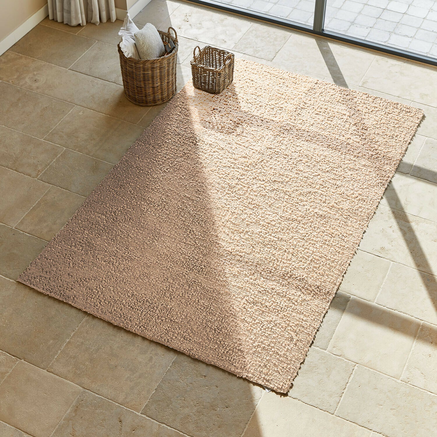 Tappeto Wodaha Tappeto beige in materiale morbido su pavimento in pietra chiara con cesti in vimini accanto