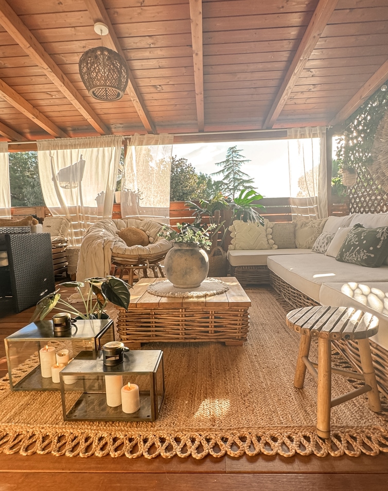 Terrazza accogliente con mobili in rattan, tavolo in legno, tappeto naturale e decorazioni con piante