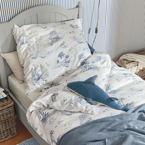 Biancheria da letto in cotone bianco con motivi marini blu su letto grigio con cuscino decorativo a forma di squalo