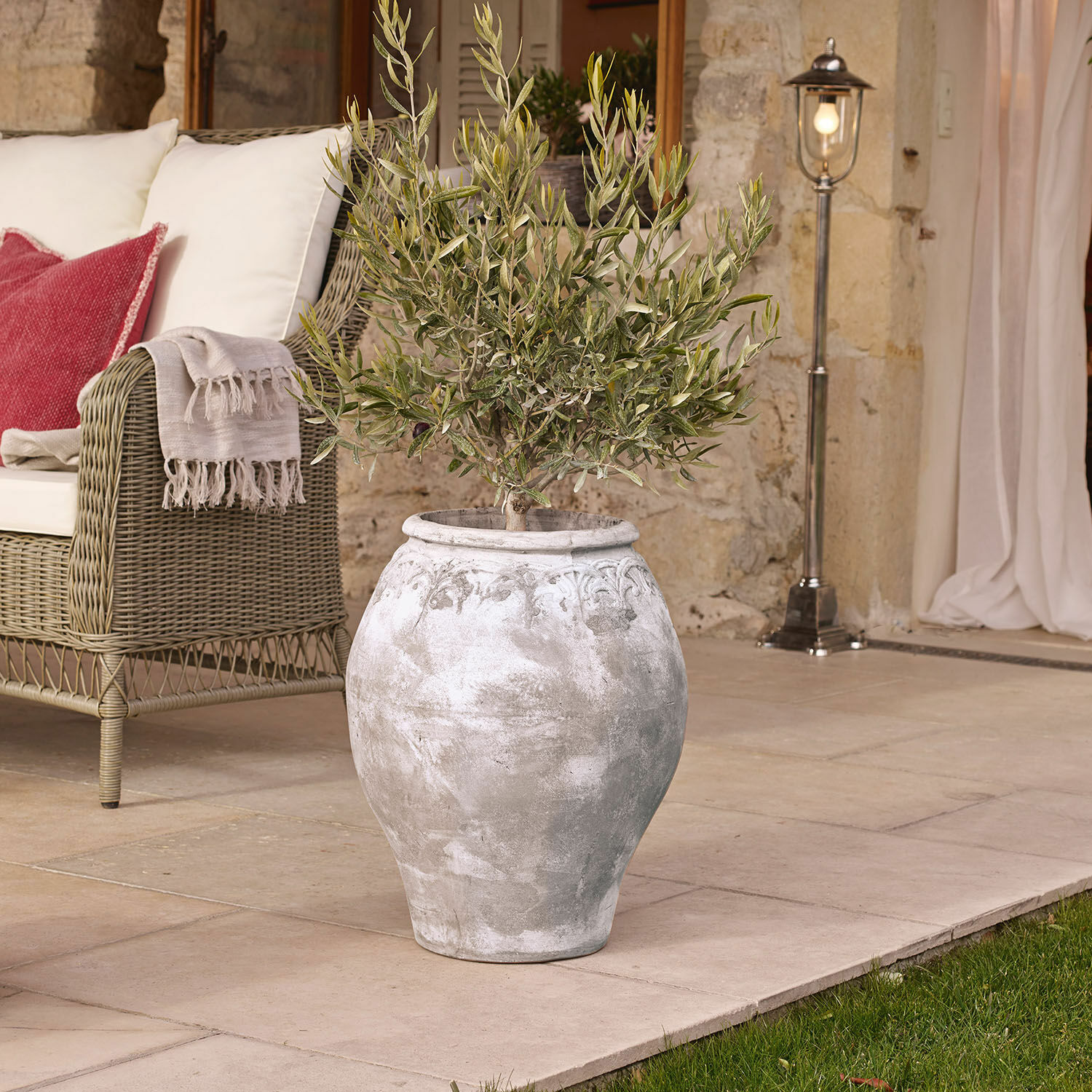 Portavaso Donneville Grande vaso in ceramica grigia con pianta su terrazza accanto a divano in vimini con cuscini