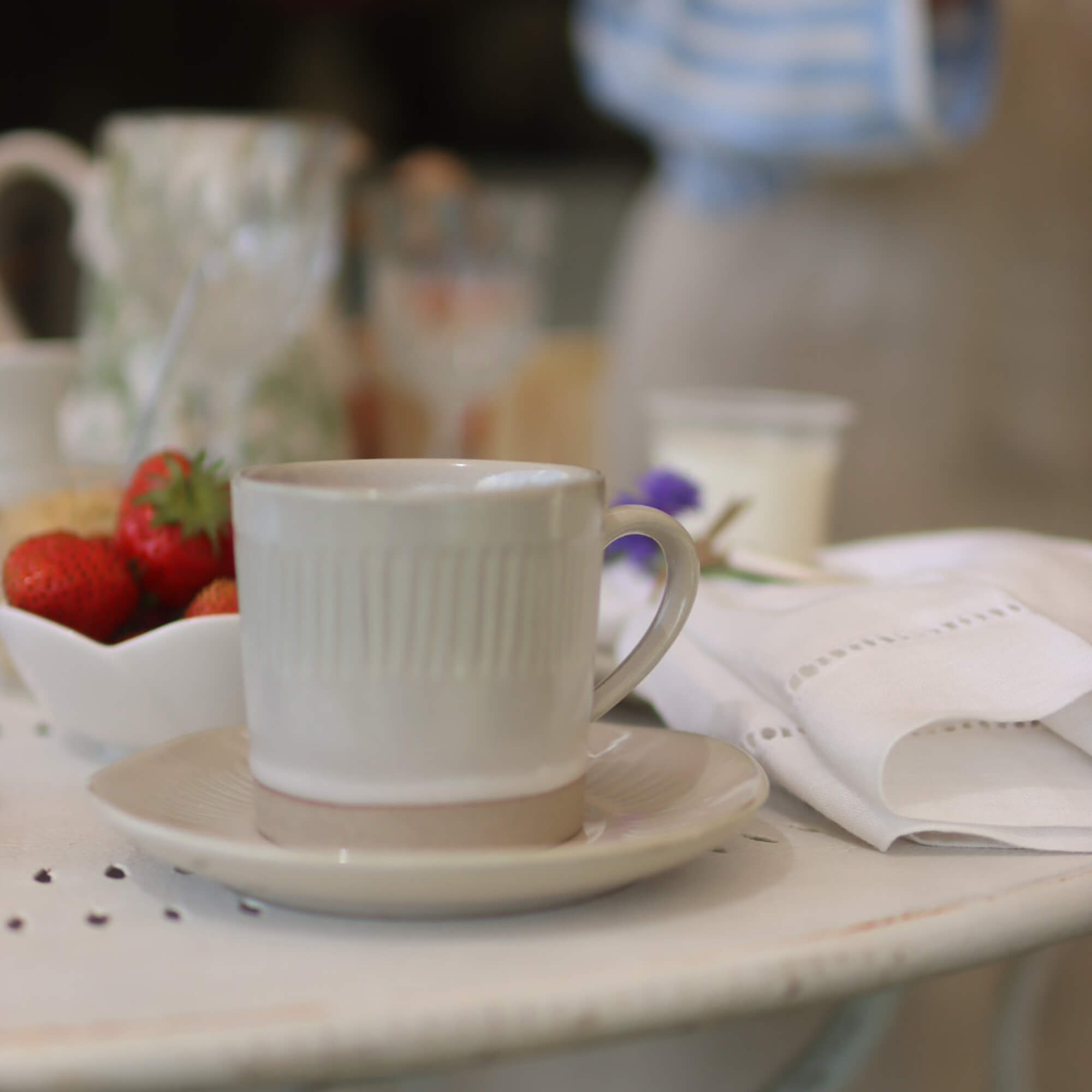 Tazza in ceramica beige con piattino su tavolo bianco con fragole e tovagliolo di lino