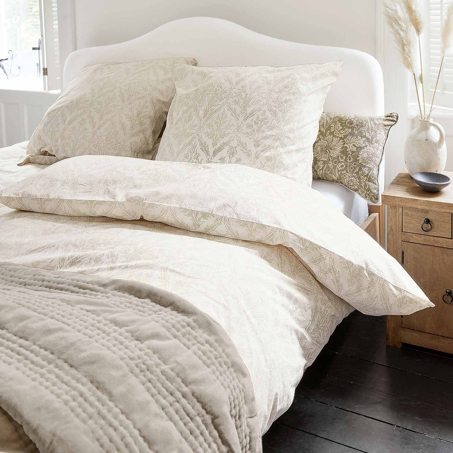 Lenzuola di cotone chiaro con delicata fantasia vegetale e coperta morbida in camera accogliente