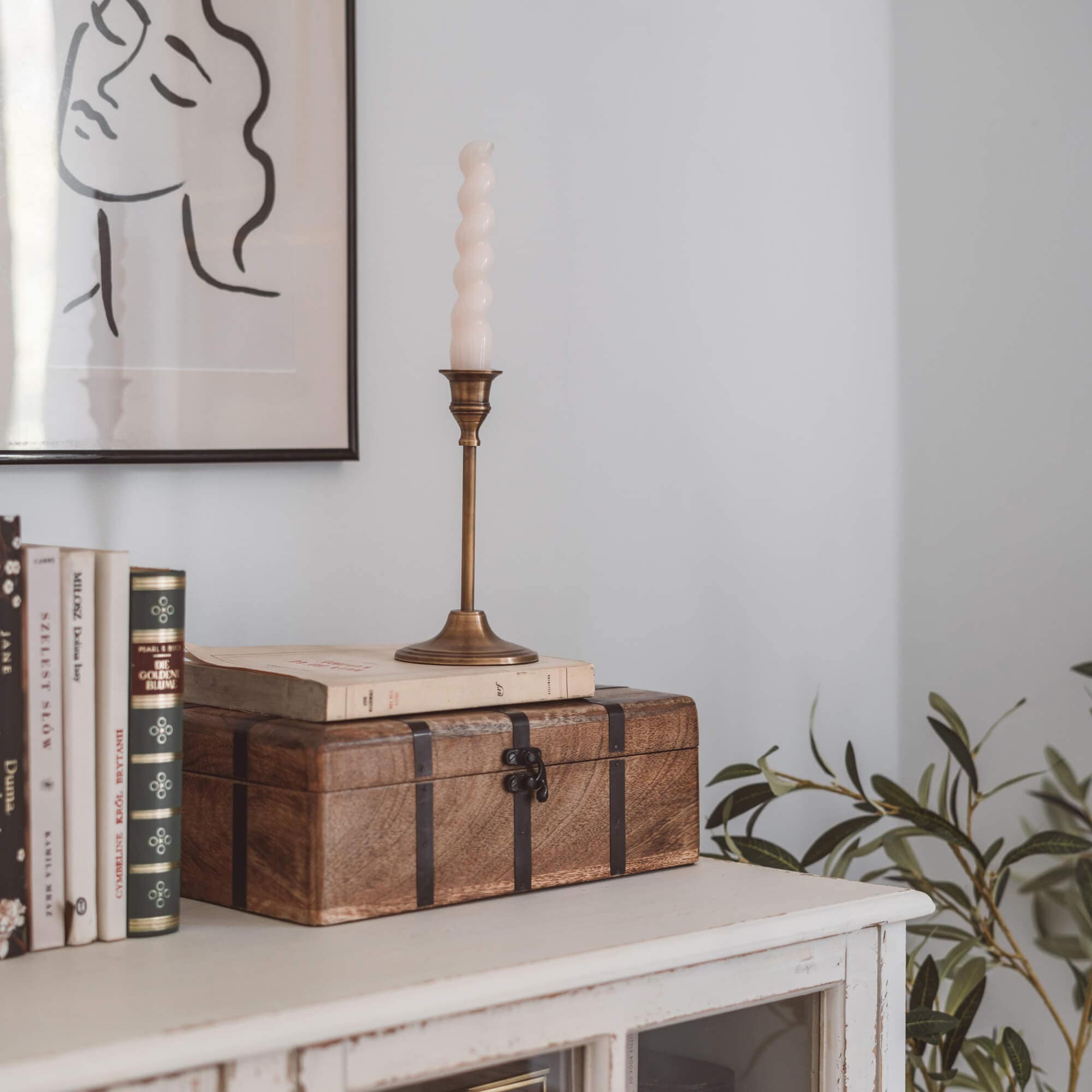 Scatola di legno marrone con fasce metalliche su mobile bianco con libri e candela