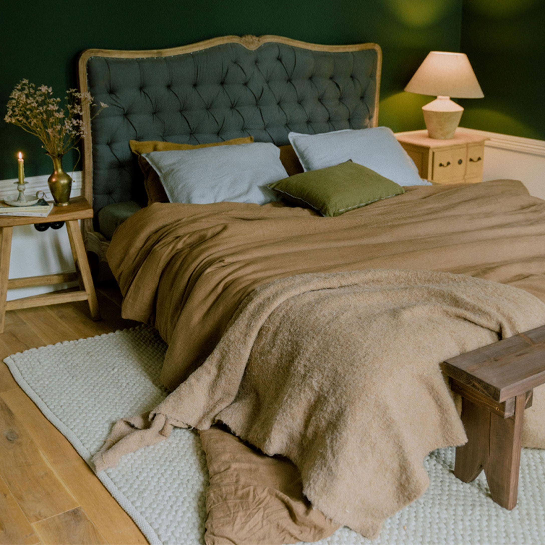 Letto accogliente con testiera imbottita verde e biancheria da letto marrone in camera