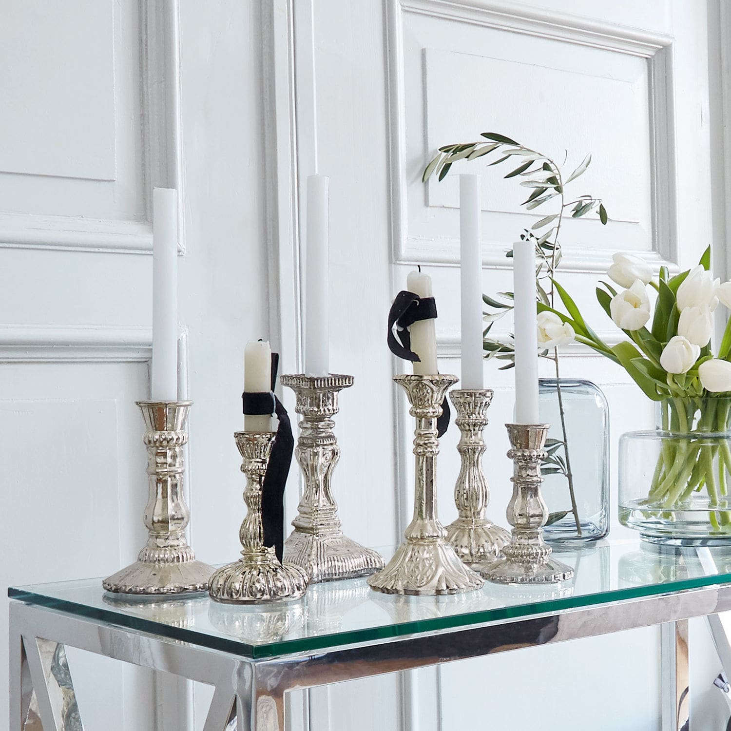 Set di 6 portacandele Adolpha Set di candelabri in metallo argentato con candele bianche su tavolo in vetro in interno luminoso