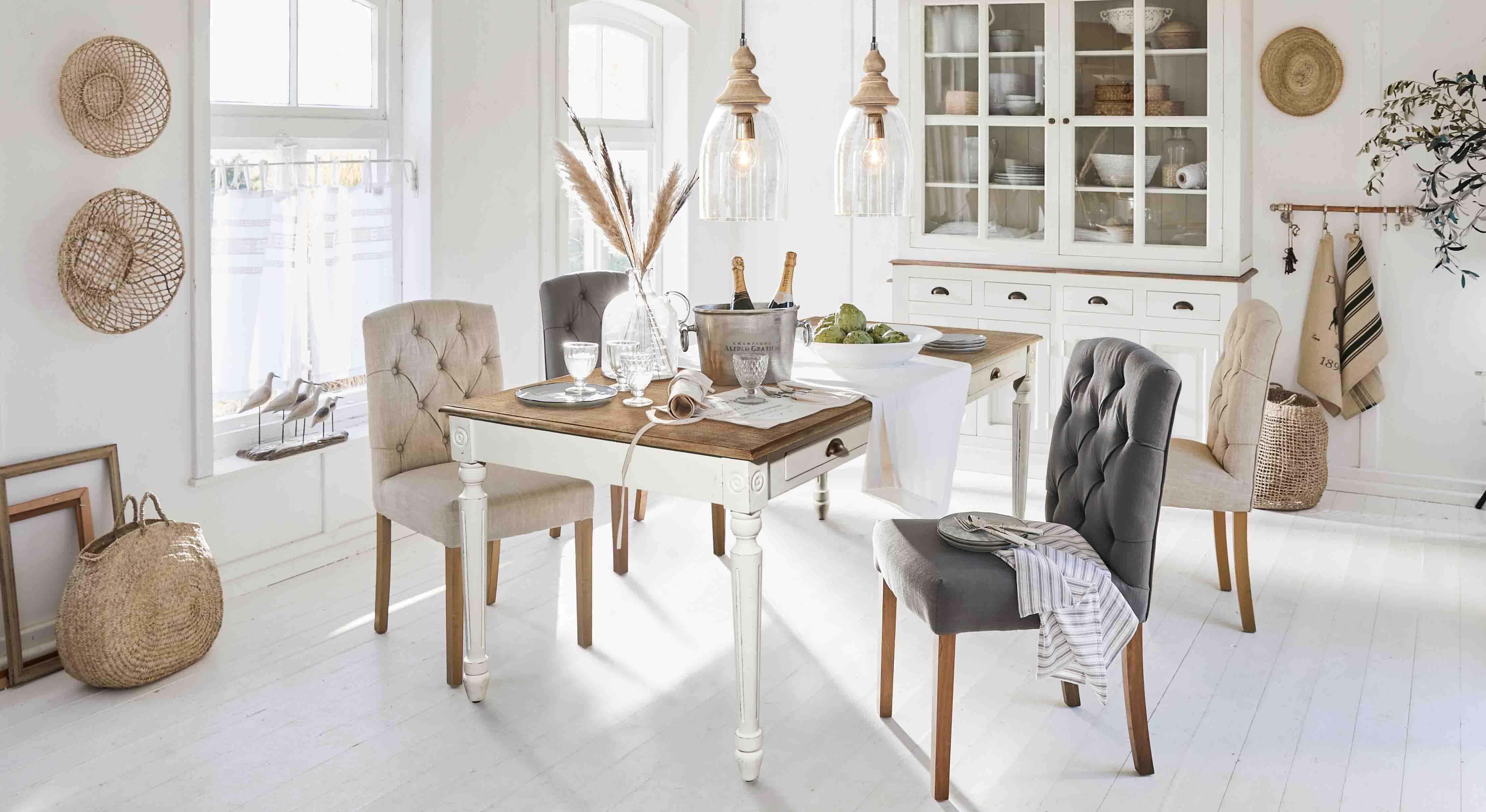 Sala da pranzo rustica con tavolo in legno bianco e sedie imbottite beige e grigie in ambiente luminoso