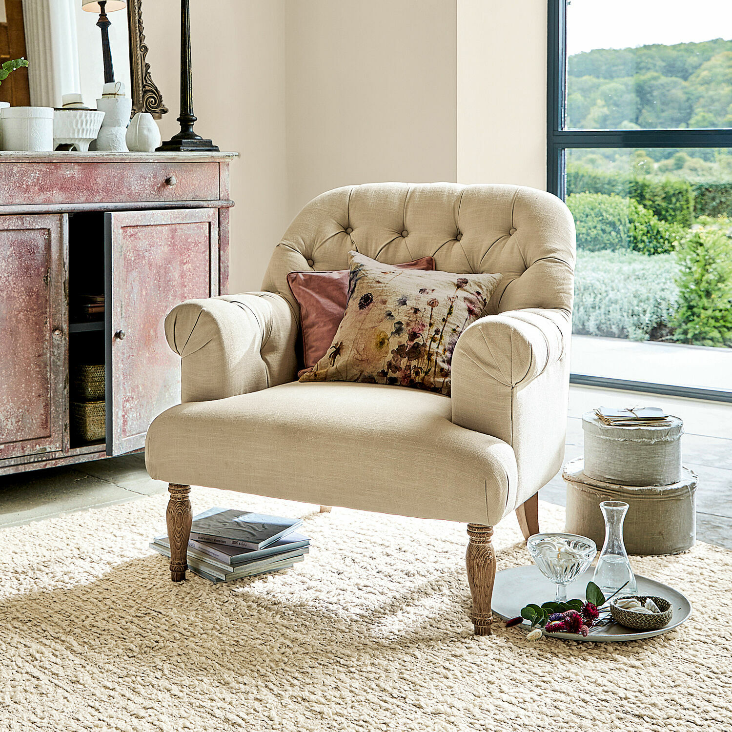 Poltrona Shambrook Poltrona beige imbottita con gambe in legno e cuscini decorativi in soggiorno luminoso