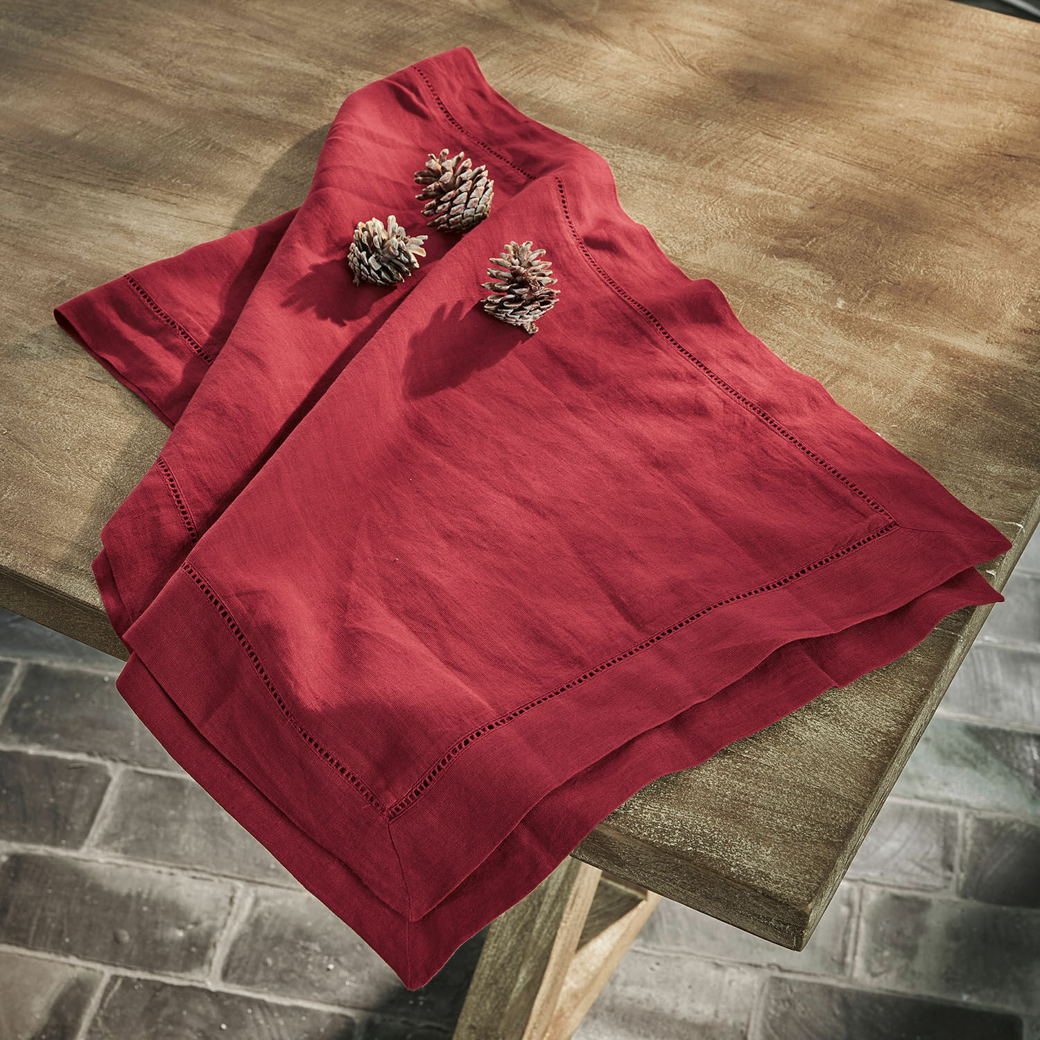 Runner Covent Garden Tovaglia in lino rosso con cuciture decorative su tavolo in legno, decorata con pigne