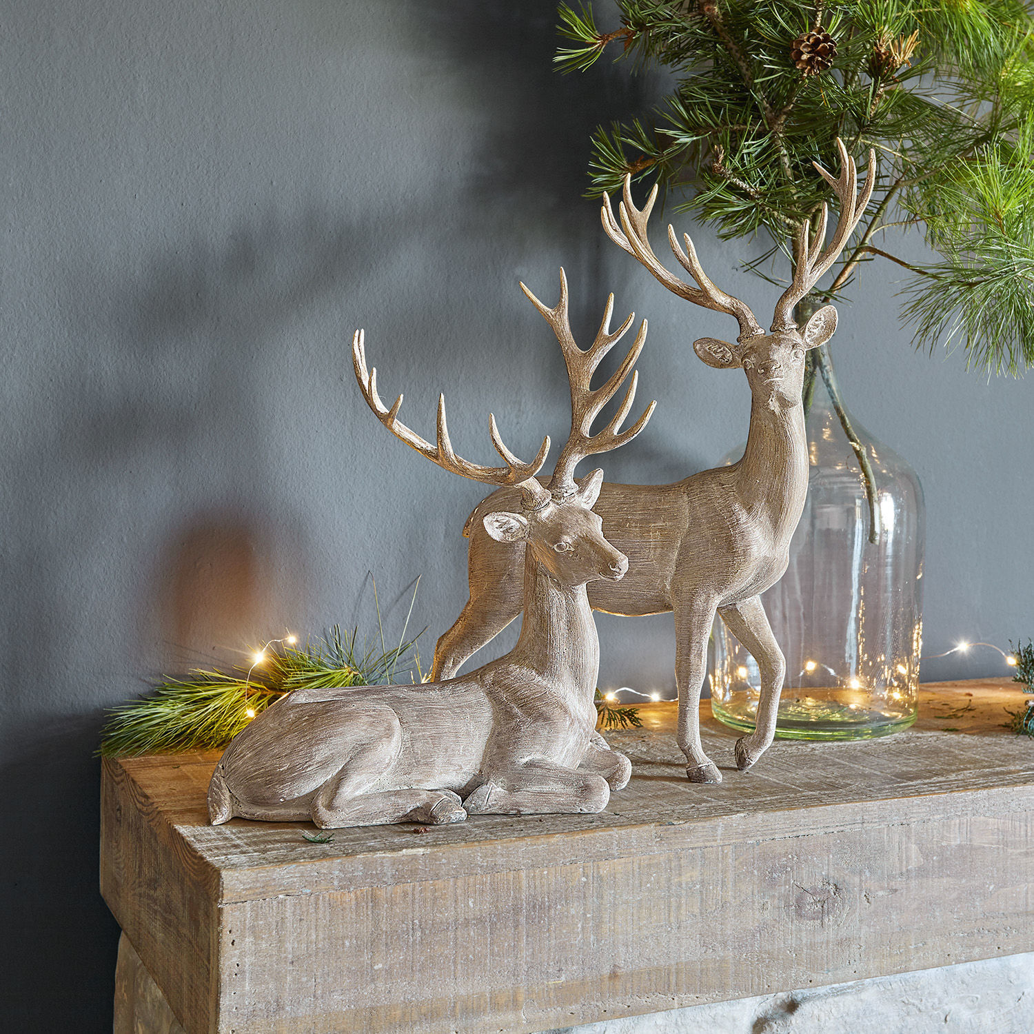 Coppia di cervi Barima Due figure decorative di cervi in legno colore naturale su piano in legno con rami verdi