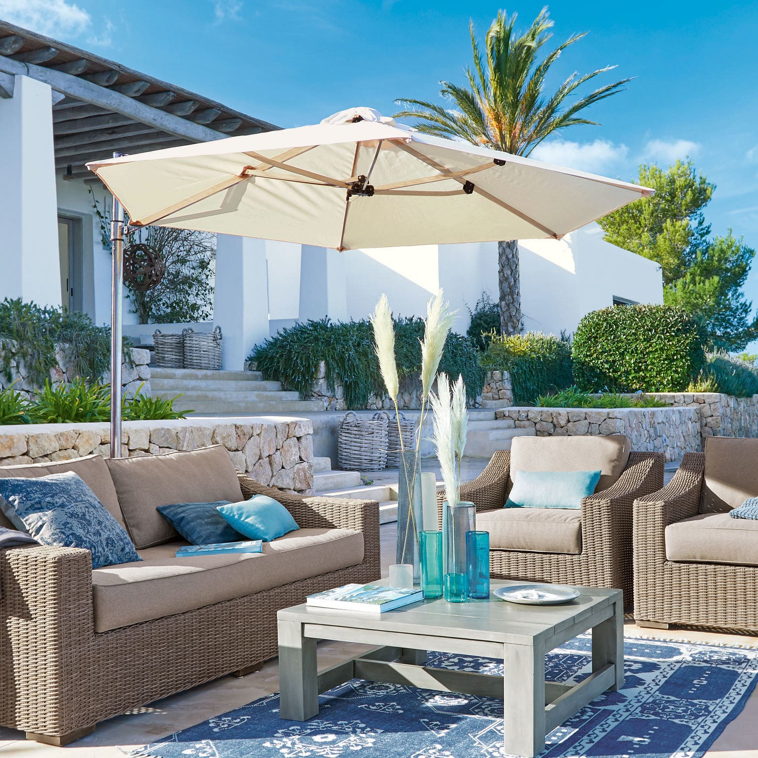 Ombrellone Boudicca Set di mobili da giardino in rattan sintetico beige con ombrellone crema su terrazza con tappeto blu