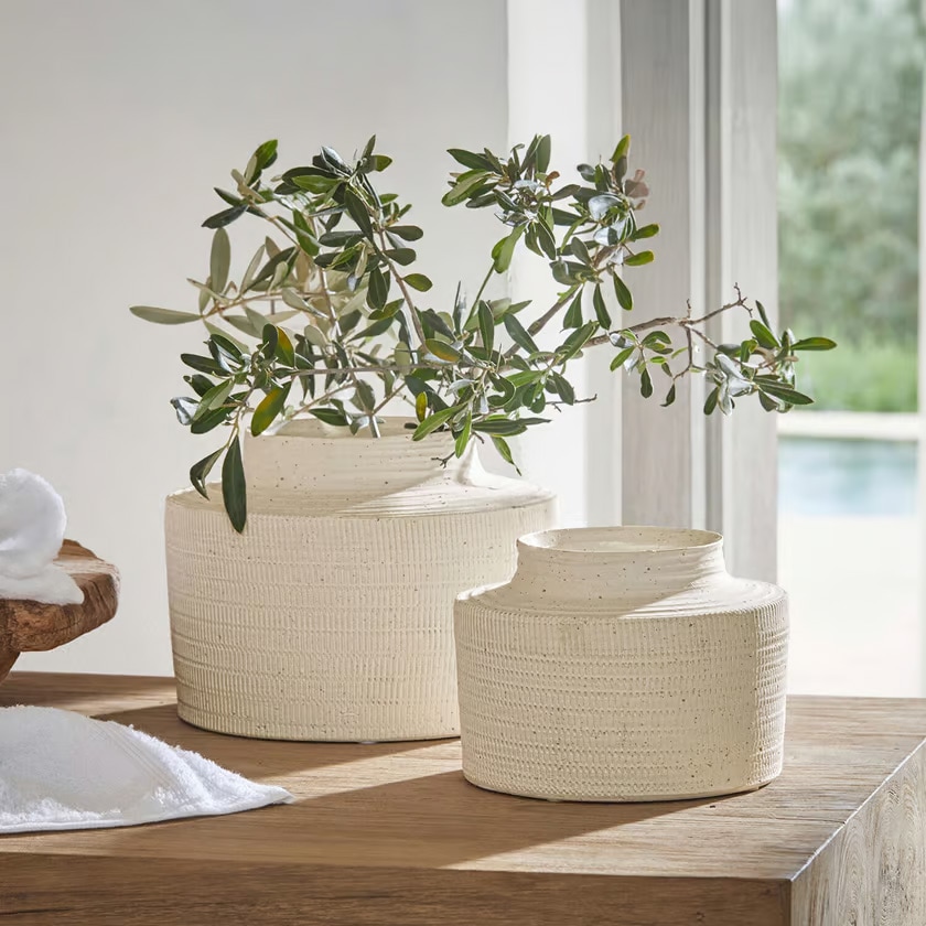 Due vasi in ceramica crema con texture su tavolo in legno con rami verdi decorativi