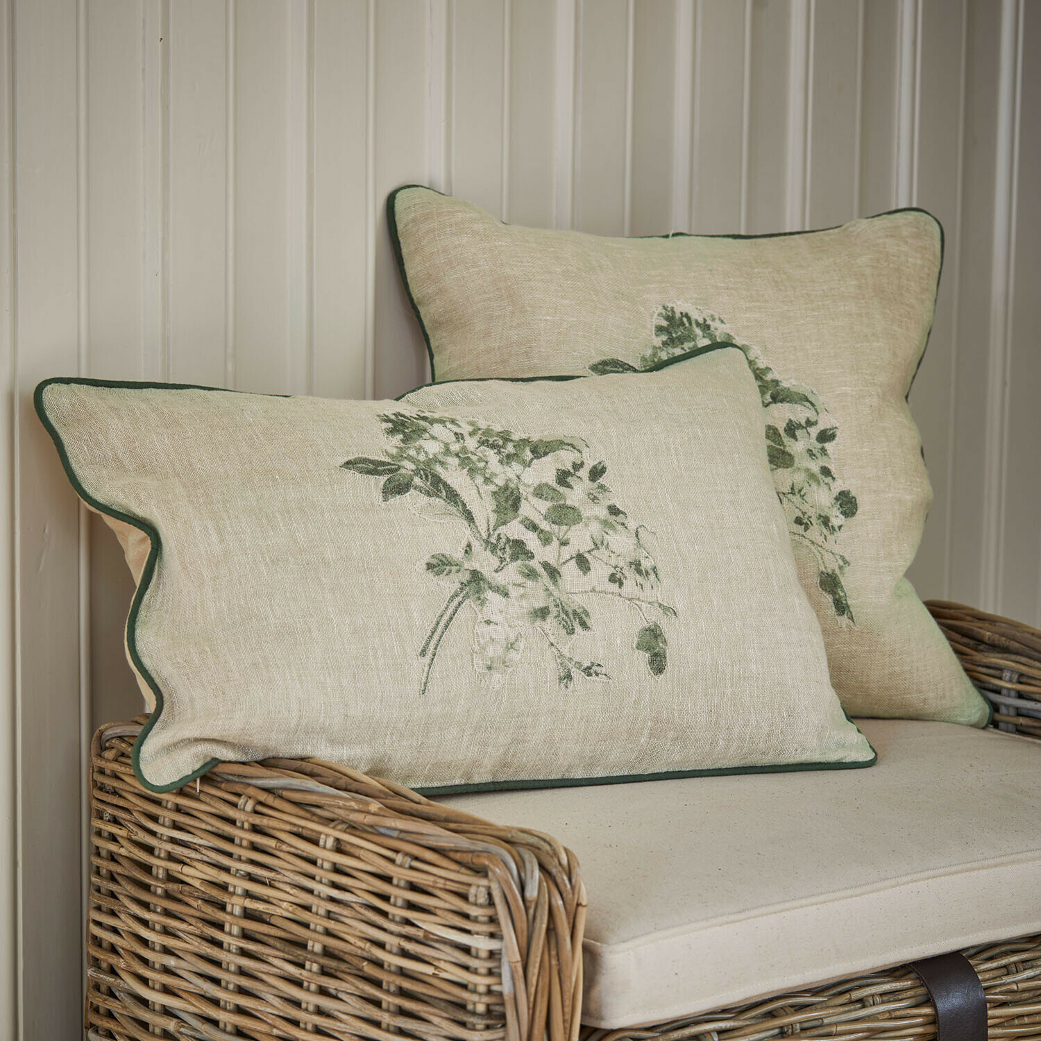 Coppia di copricuscini Chantrelle Cuscini in lino beige con stampa vegetale verde e bordo verde su divano in vimini