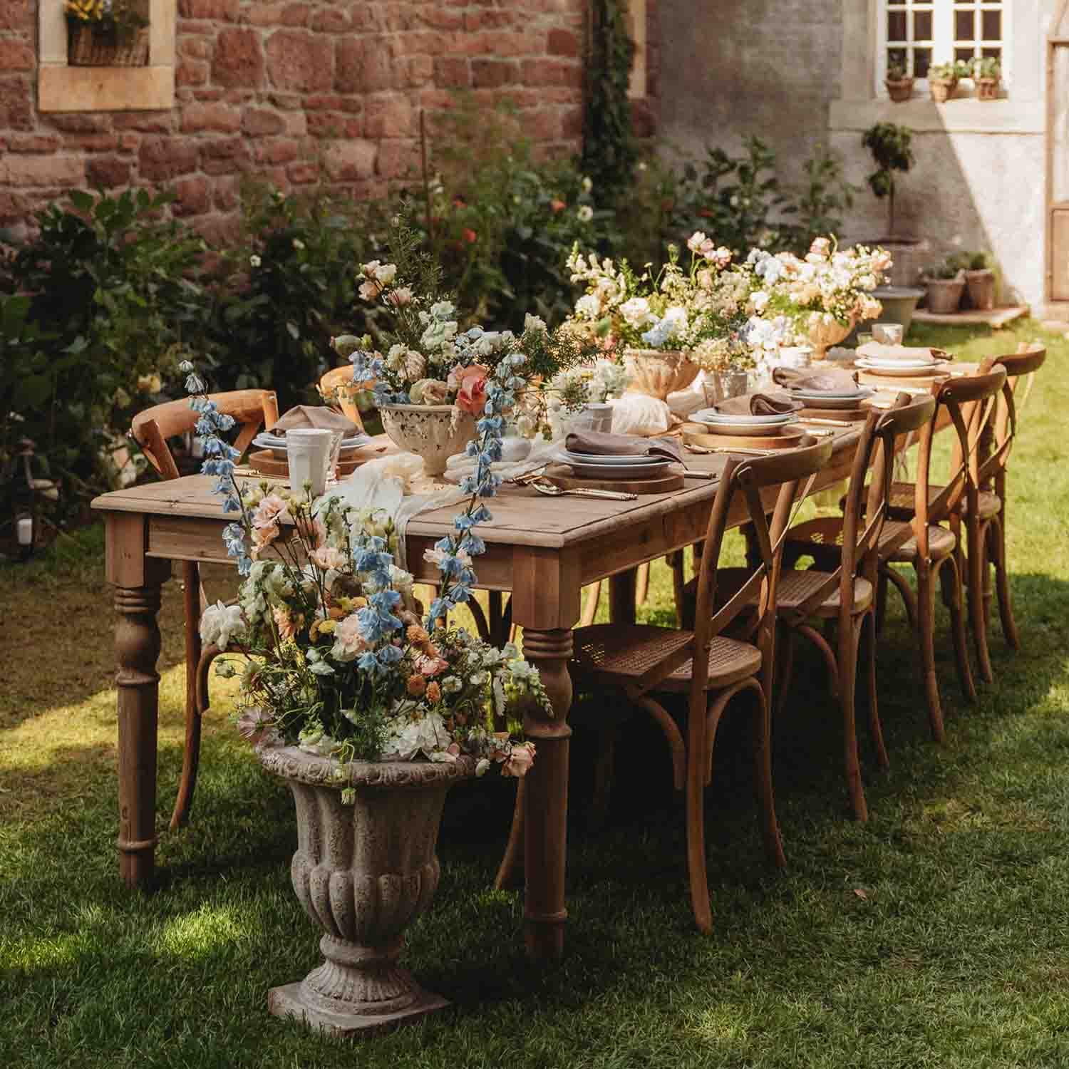 Tavolo in legno da giardino con decorazioni floreali e apparecchiatura per festa all'aperto