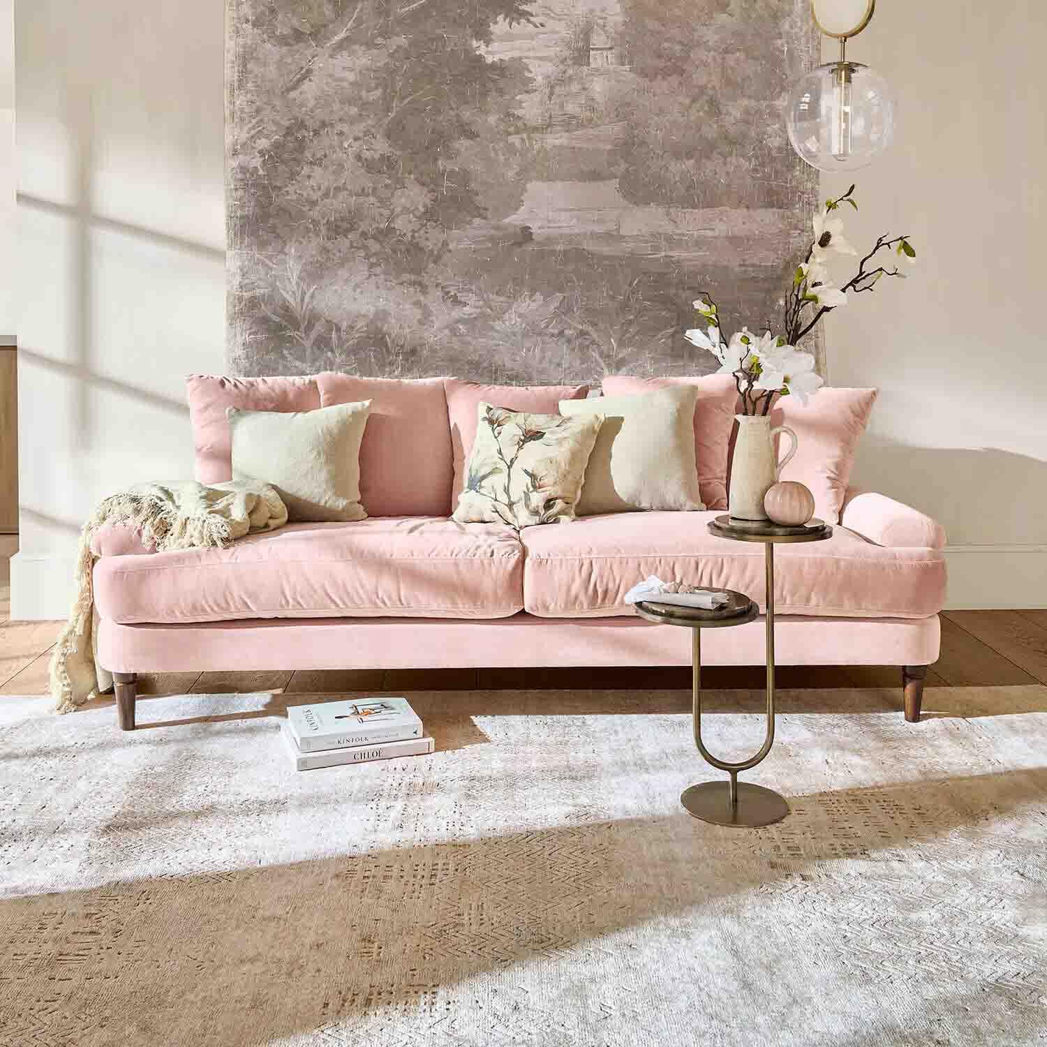 Divano in velluto rosa con cuscini e tavolino in soggiorno luminoso con decorazione murale