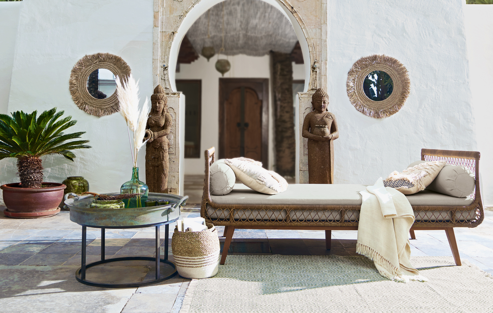 Soggiorno orientale con chaise longue in rattan beige, decorazioni in pietra e specchi in erba marina