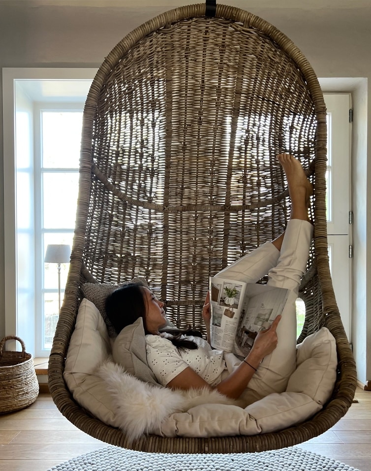 Sedia sospesa in rattan naturale con cuscini morbidi e donna che legge un libro all'interno