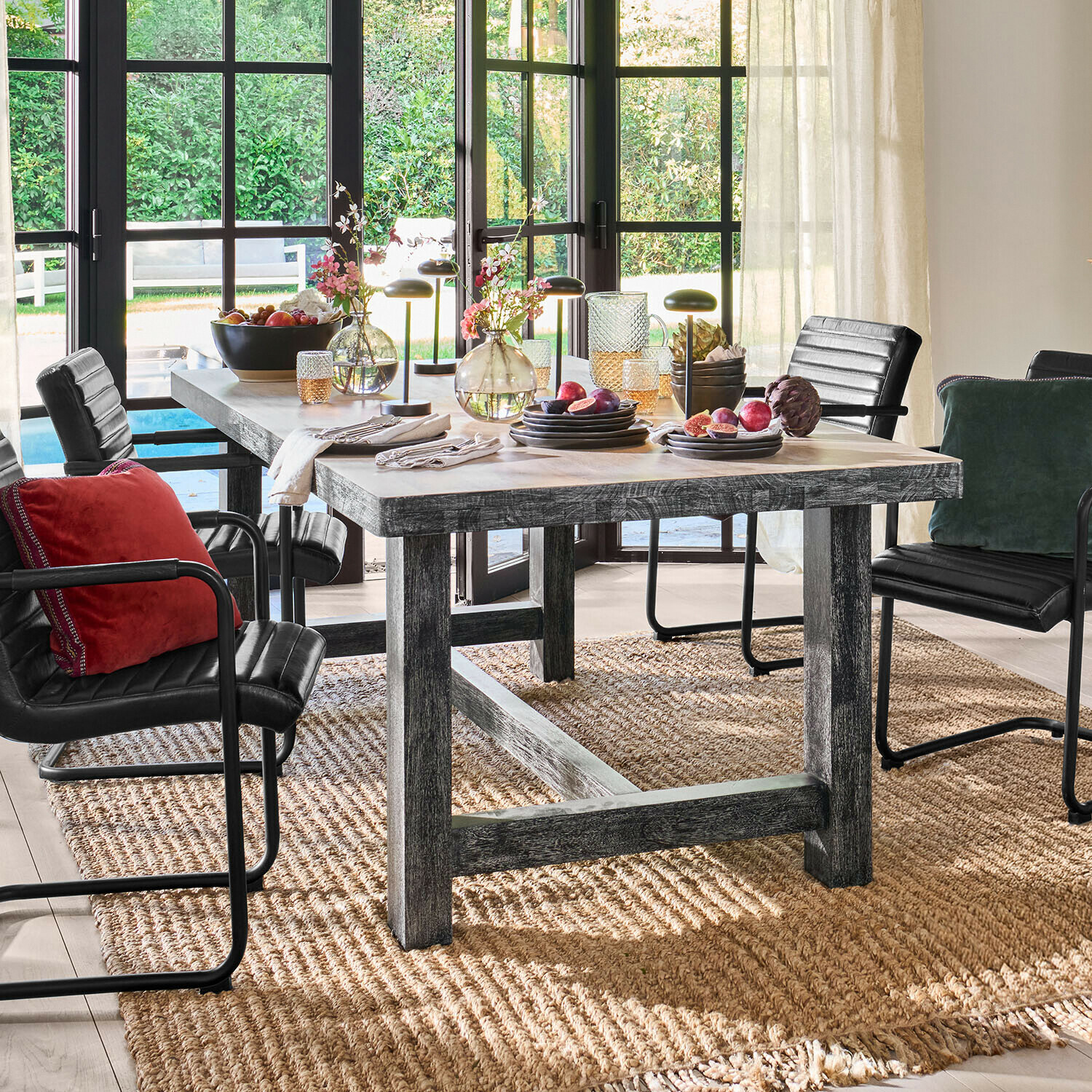 Tavolo da pranzo rustico in legno con sedie nere e decorazioni su tappeto naturale in ambiente luminoso