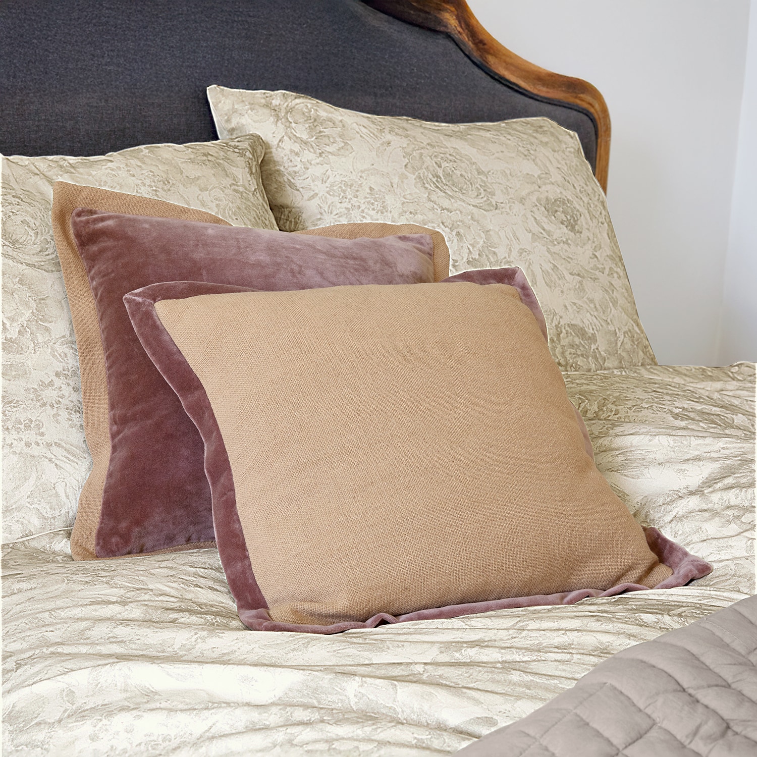 Cuscini decorativi beige e rosa in velluto e tessuto su letto con biancheria chiara