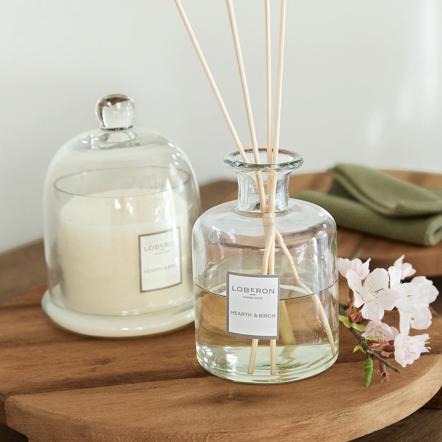 Set di profumatori per ambienti Vanis Diffusore di profumo in vetro Hearth & Birch con bastoncini su tavolo in legno e candela bianca sotto campana