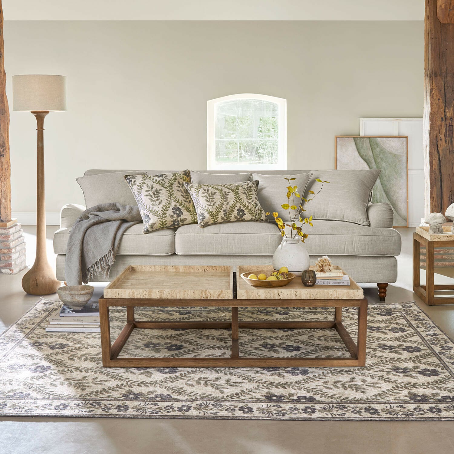 Divano beige in tessuto con cuscini decorativi e tavolino in legno su tappeto a motivi in soggiorno luminoso