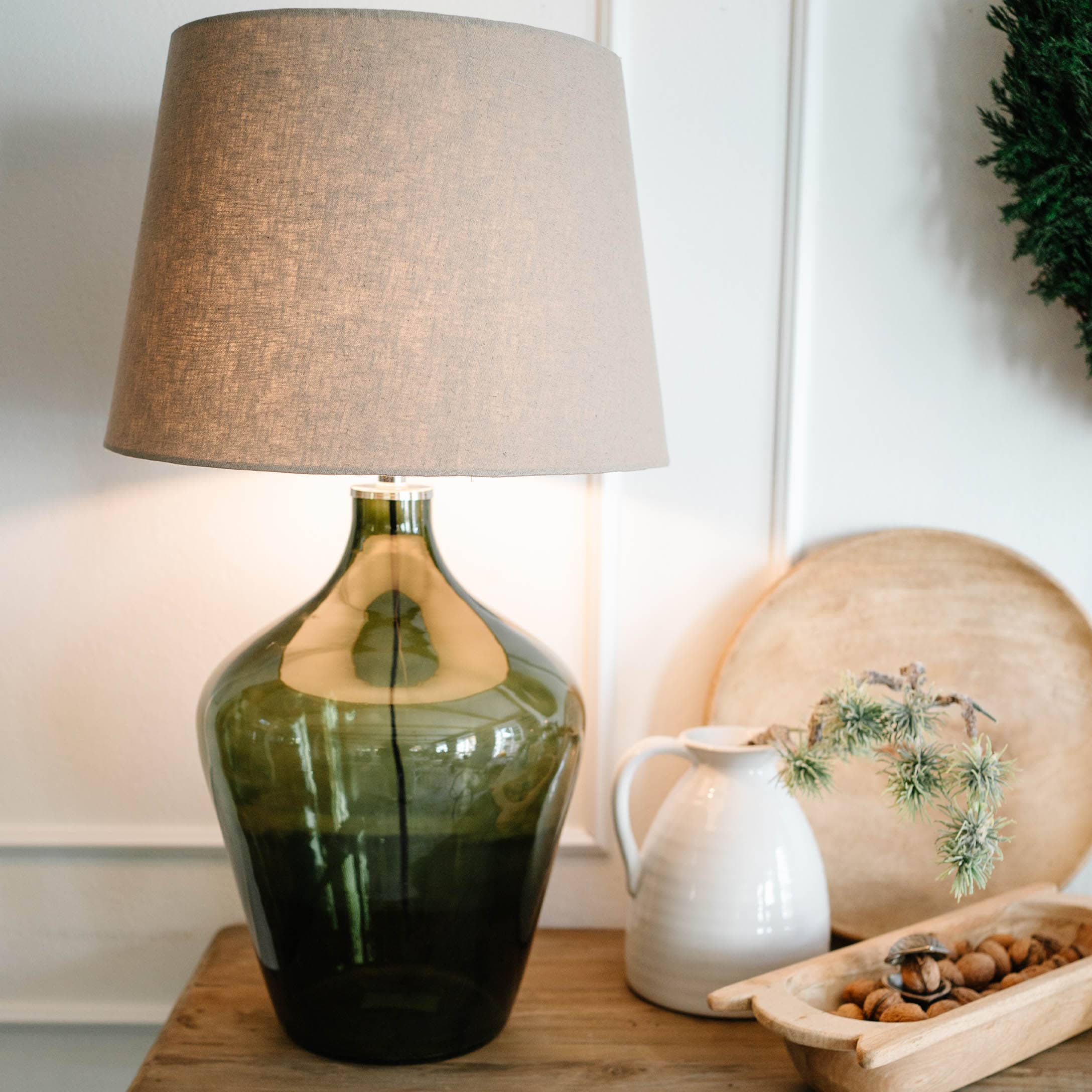 Lampada da tavolo in vetro verde con paralume beige su tavolo in legno con decorazioni