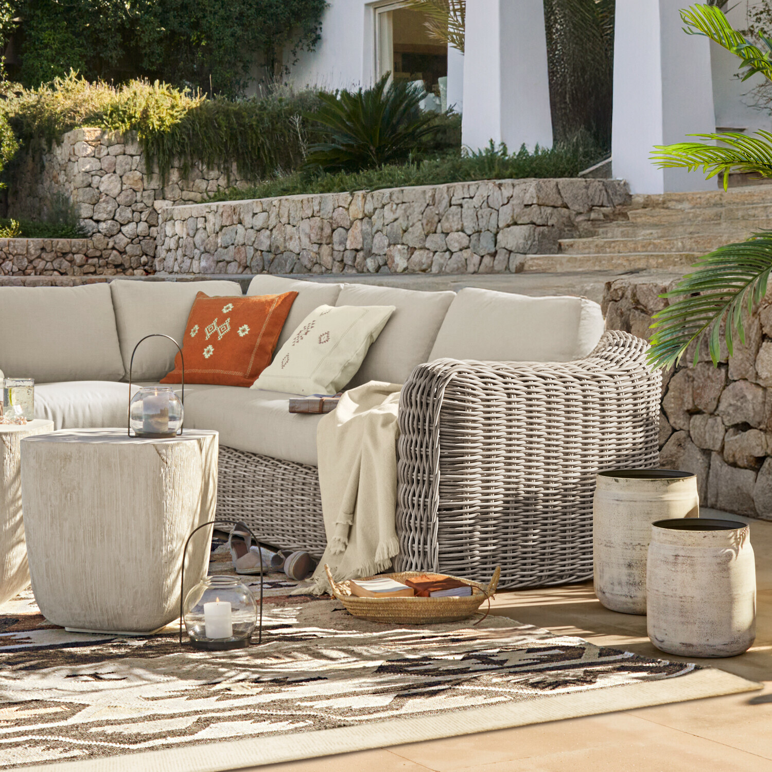 Set di mobili da giardino in rattan grigio con cuscini beige su terrazza con muro in pietra