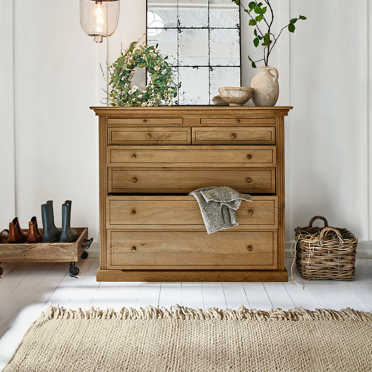 Cassettiera in legno naturale con più cassetti, decorazioni e tappeto chiaro in interno luminoso