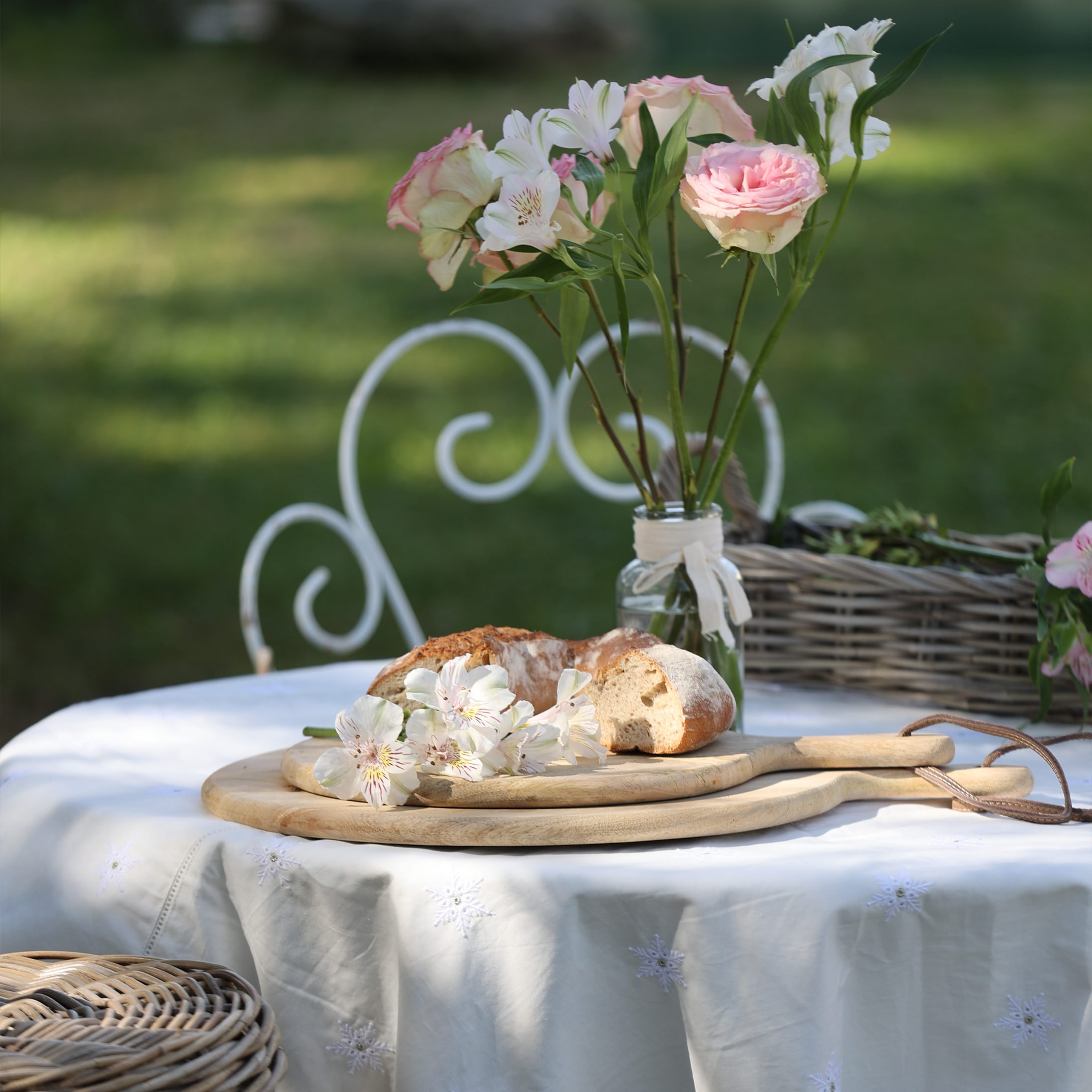 Tagliere in legno con pane e fiori su tovaglia bianca in giardino