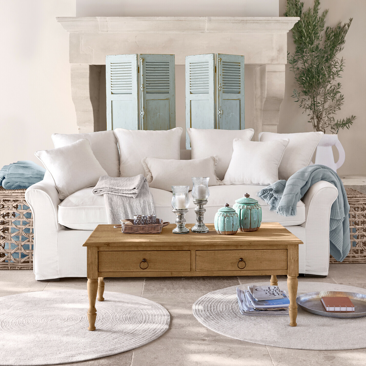 Divano beige con cuscini e tavolino in legno con decorazioni in soggiorno luminoso con camino