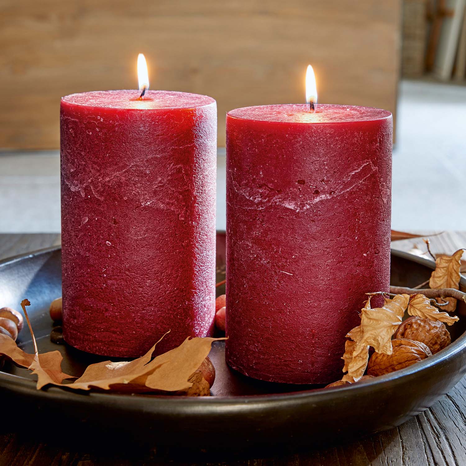 Due candele rosse in cera naturale su un vassoio nero con foglie secche e noci decorative