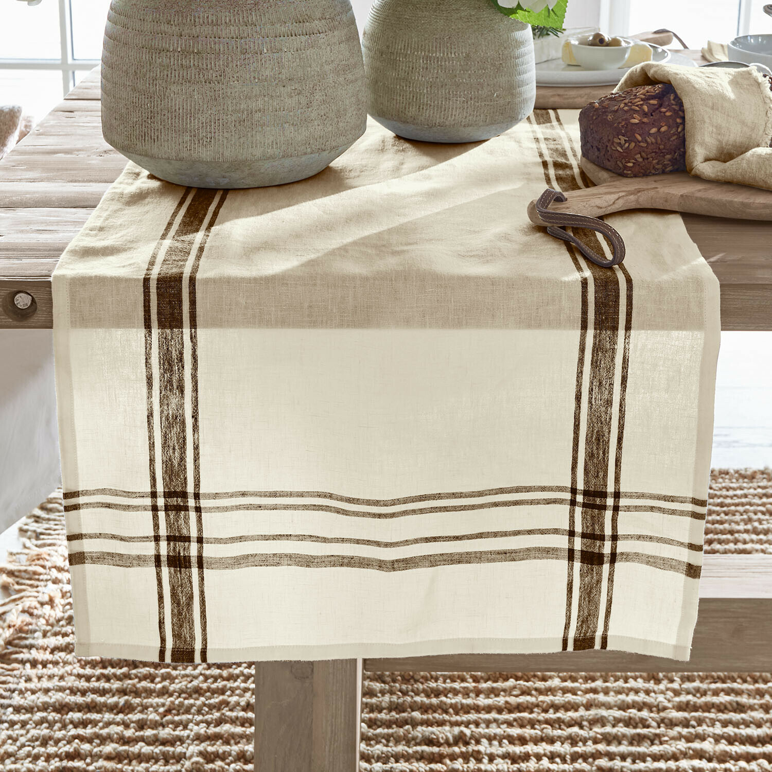 Runner Ellory Runner da tavola in lino beige con strisce marroni su tavolo in legno, decorato con pane e stoviglie