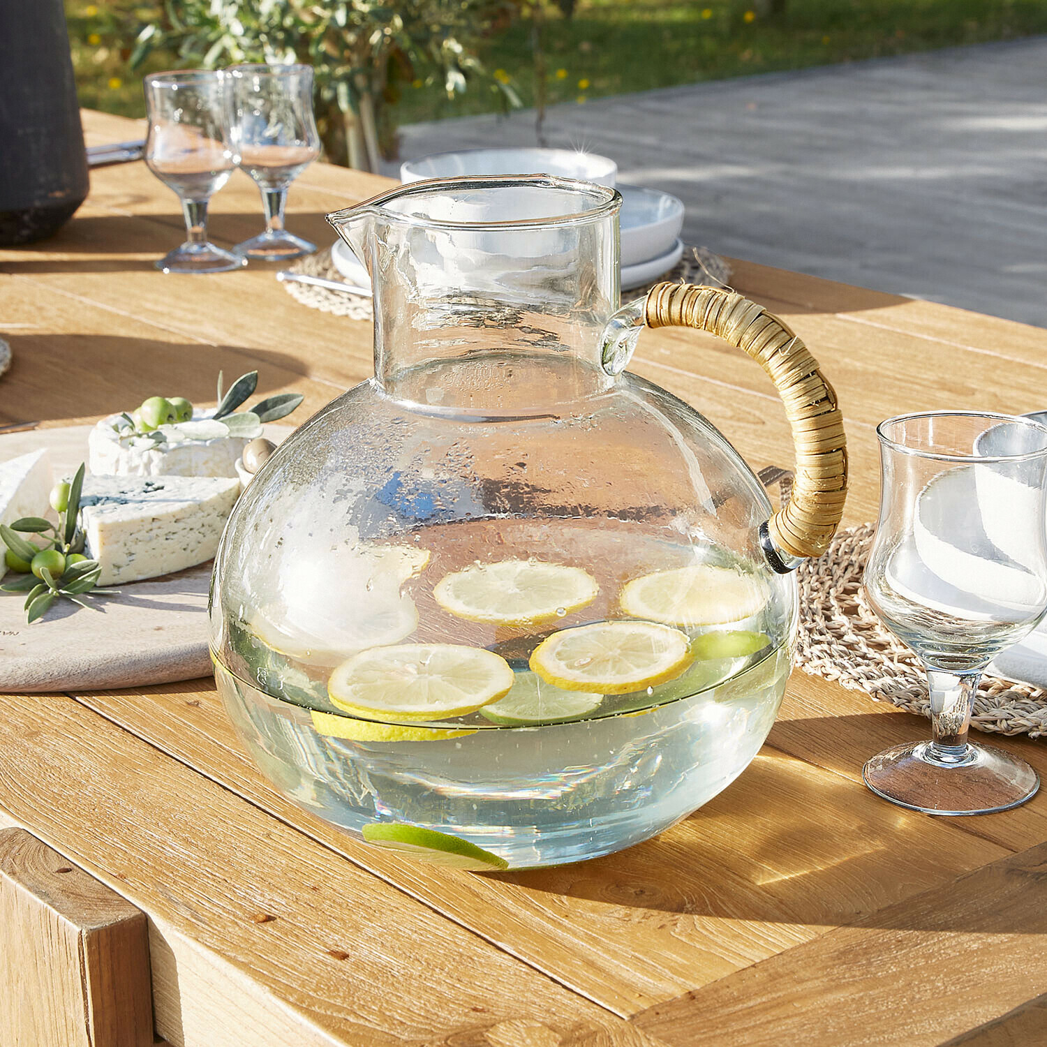 Caraffa Stormea Brocca in vetro con manico in rattan su tavolo in legno, acqua con fette di limone e lime
