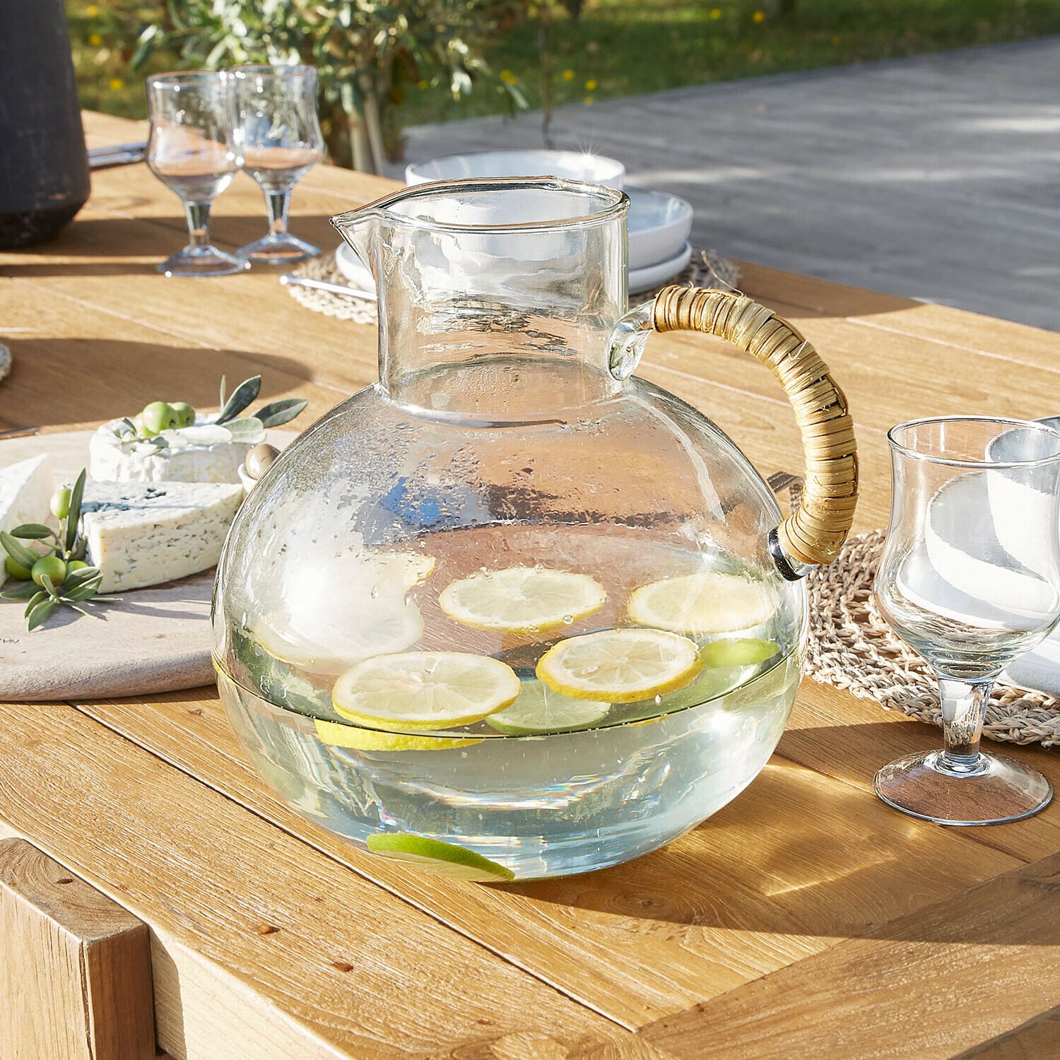Caraffa Stormea Brocca in vetro con manico in rattan su tavolo in legno, acqua con fette di limone e lime