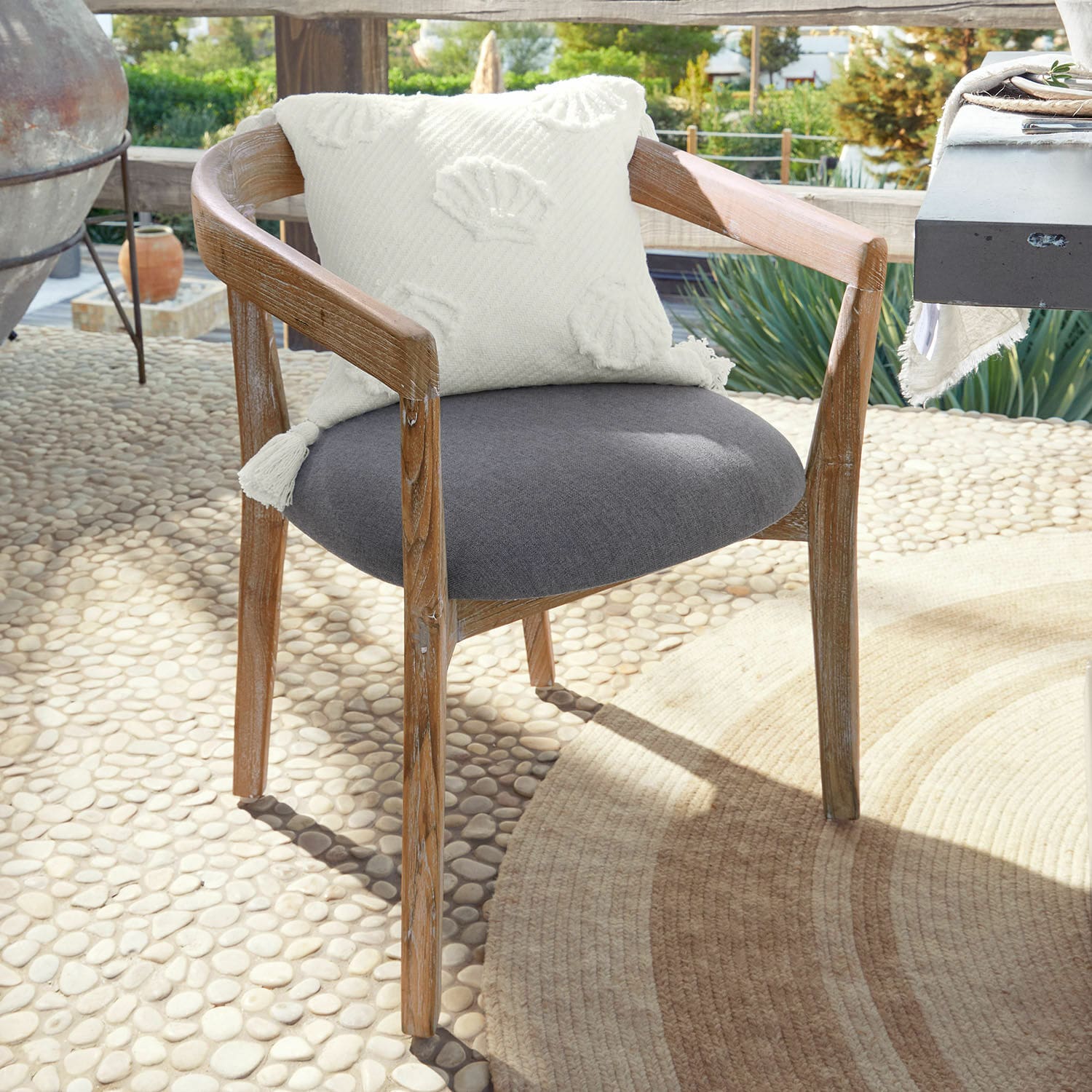 Sedia Lunebois Sedia in legno con seduta grigia imbottita e cuscino decorativo bianco su terrazza soleggiata