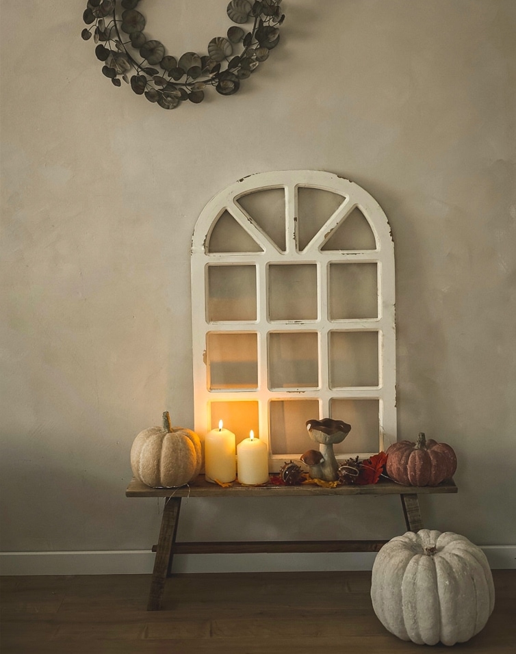 Zucca decorativa e candele su panca in legno con cornice finestra bianca su parete beige
