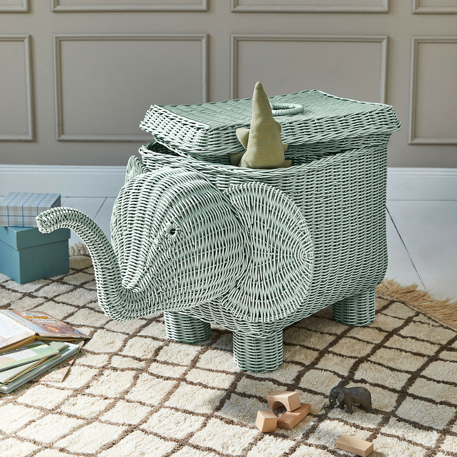 Cesto in rattan verde menta a forma di elefante con coperchio aperto e giocattoli sul tappeto