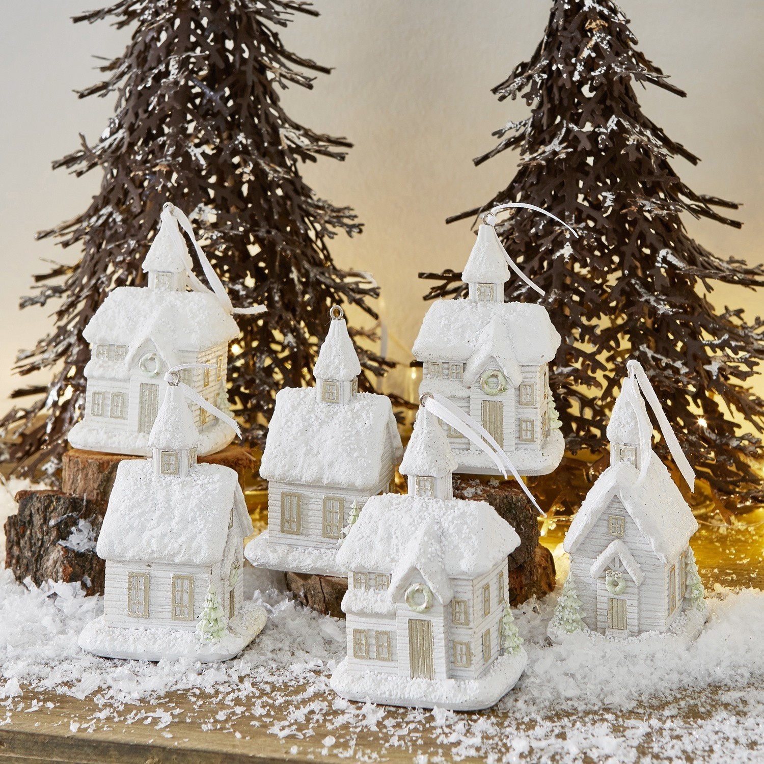 Set di 6 decorazioni natalizie Legé Decorazioni di casette bianche innevate su tavolo in legno con alberi metallici e luci natalizie