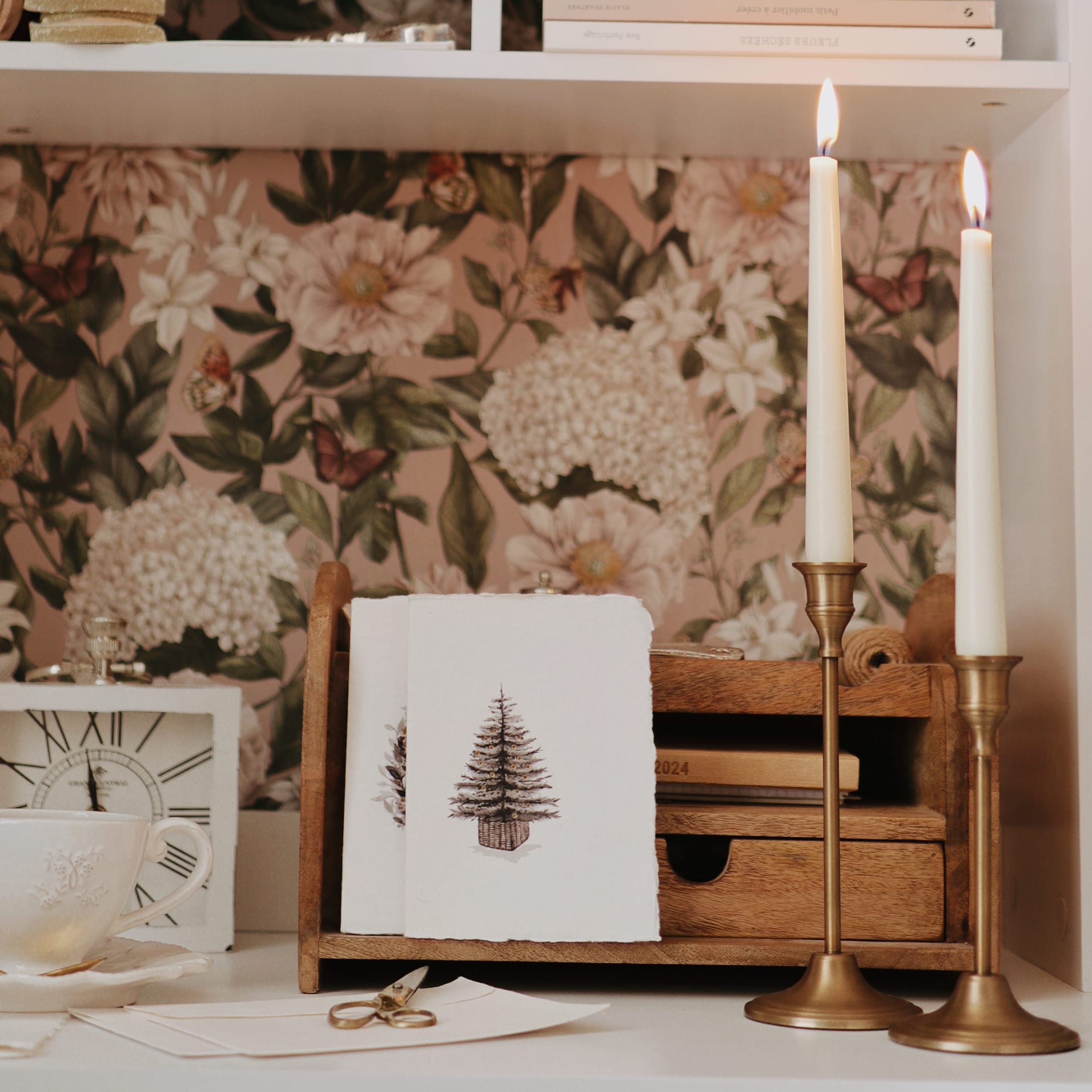 Organizer in legno con biglietti di Natale e due candelabri dorati davanti a carta da parati floreale