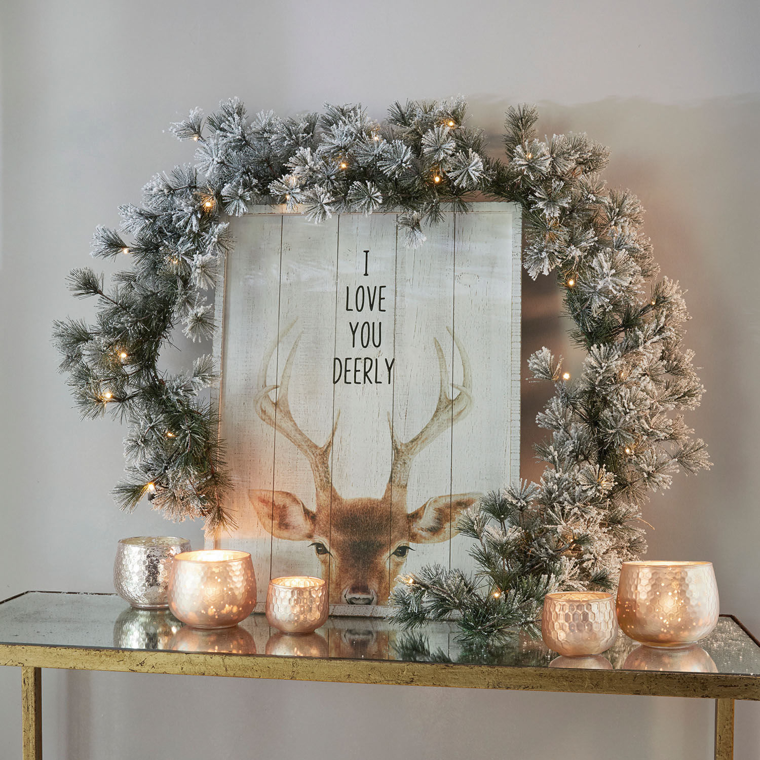 Ghirlanda Toni Corona decorativa con rami innevati e luci LED su tavolo dorato con candele accese