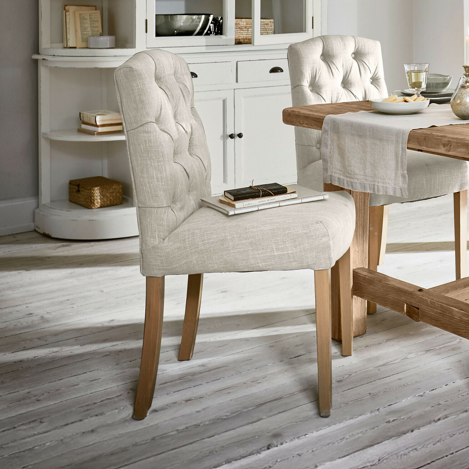 Sedia Fulden Sedia imbottita beige con gambe in legno accanto a tavolo in legno in ambiente luminoso