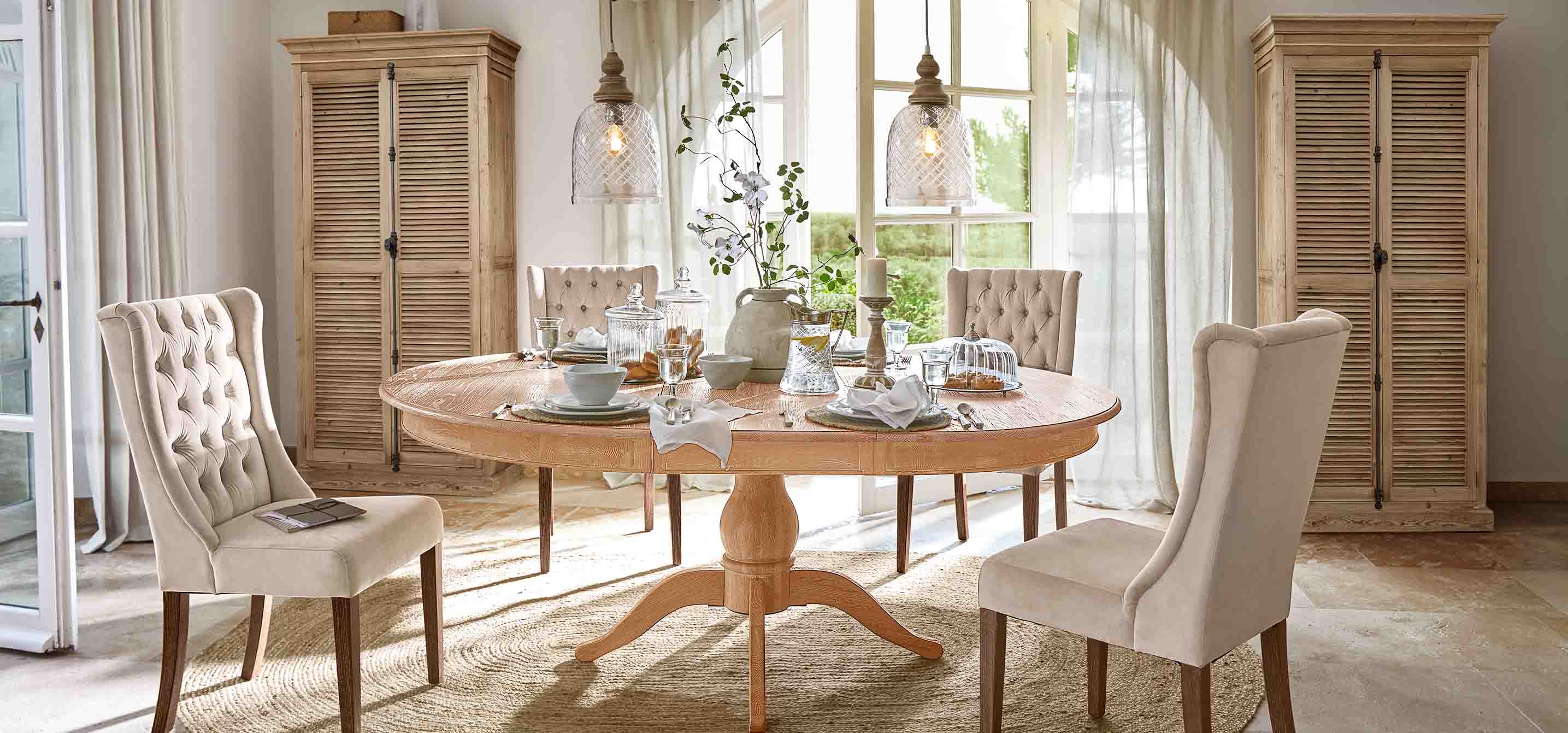 Sala da pranzo con tavolo rotondo in legno chiaro e sedie imbottite beige in stile vintage