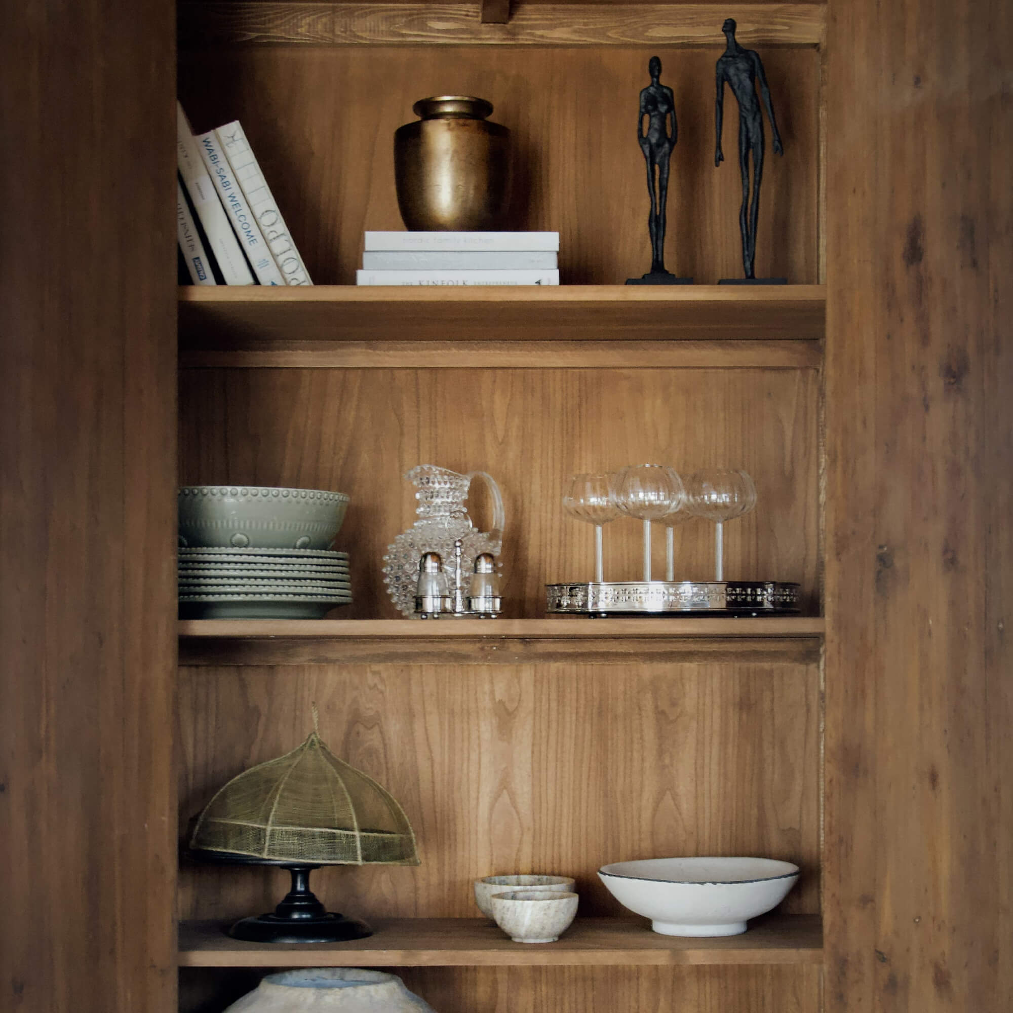 Mensola in legno con oggetti decorativi: ceramica verde, brocca di vetro e calici da vino