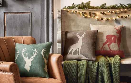 Cuscini decorativi con motivo di cervo in colori naturali su poltrona in pelle e panca con coperta verde