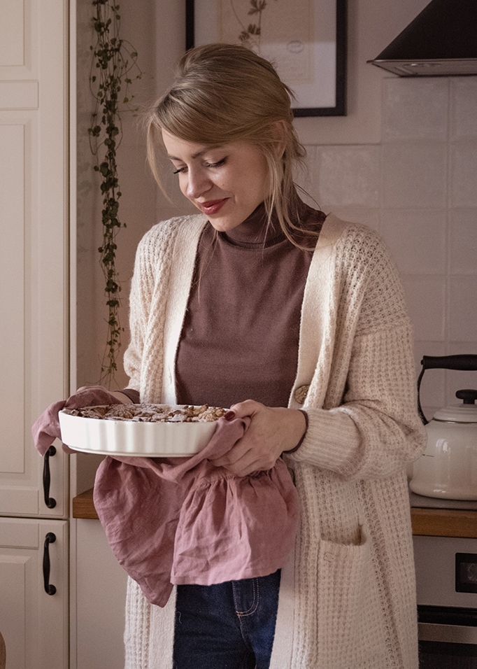 Donna con cardigan beige che tiene una teglia bianca in ceramica con panno rosa in cucina
