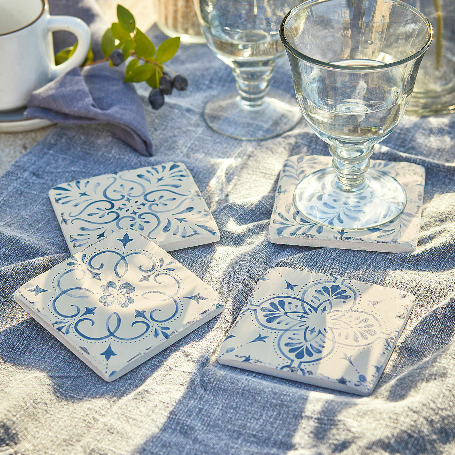 Set di 4 sottobicchieri Évry Sottobicchieri in ceramica bianca con motivo blu su tovaglia di lino blu