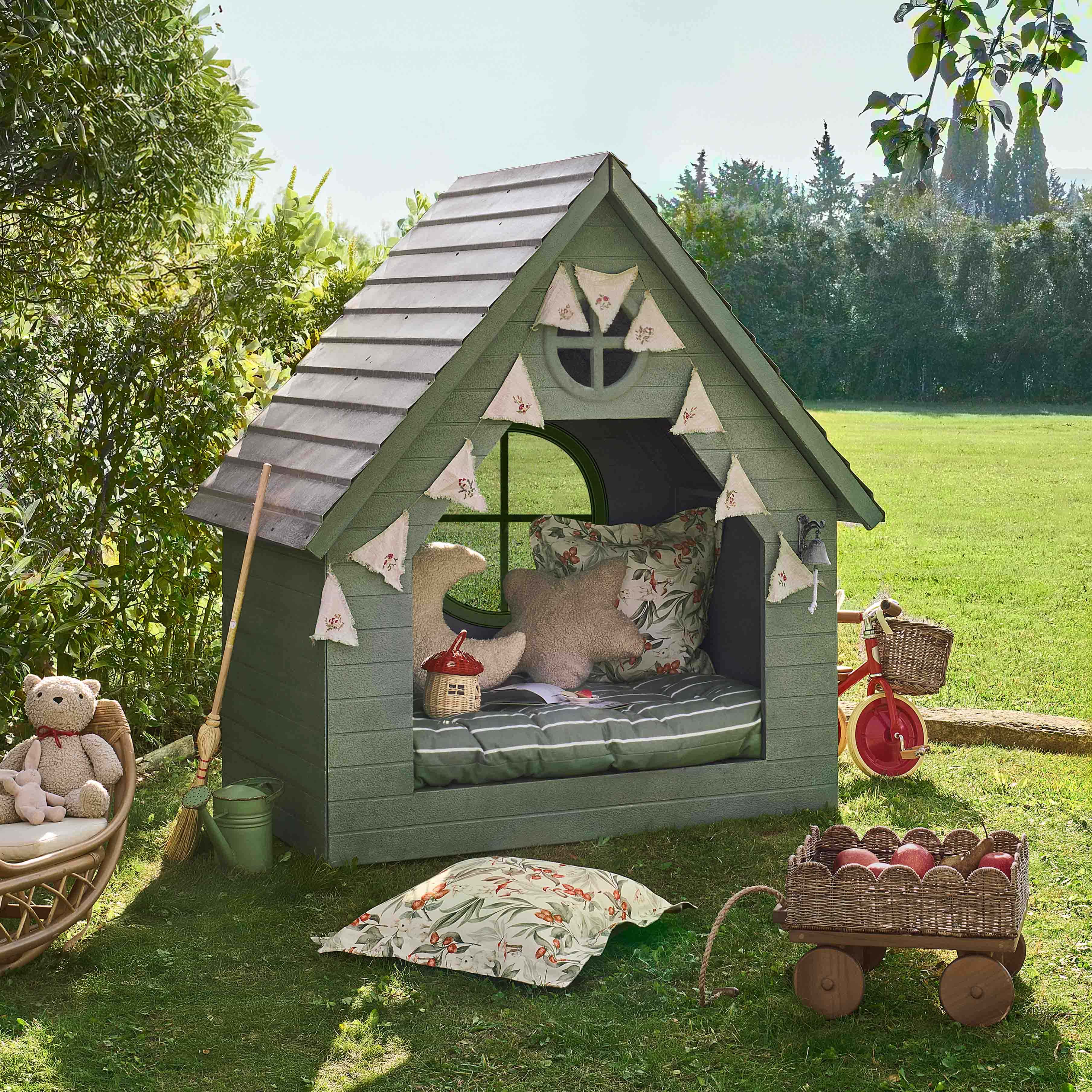 Casetta da giardino verde in legno con cuscini decorativi e ghirlanda, perfetta per giochi bambini.