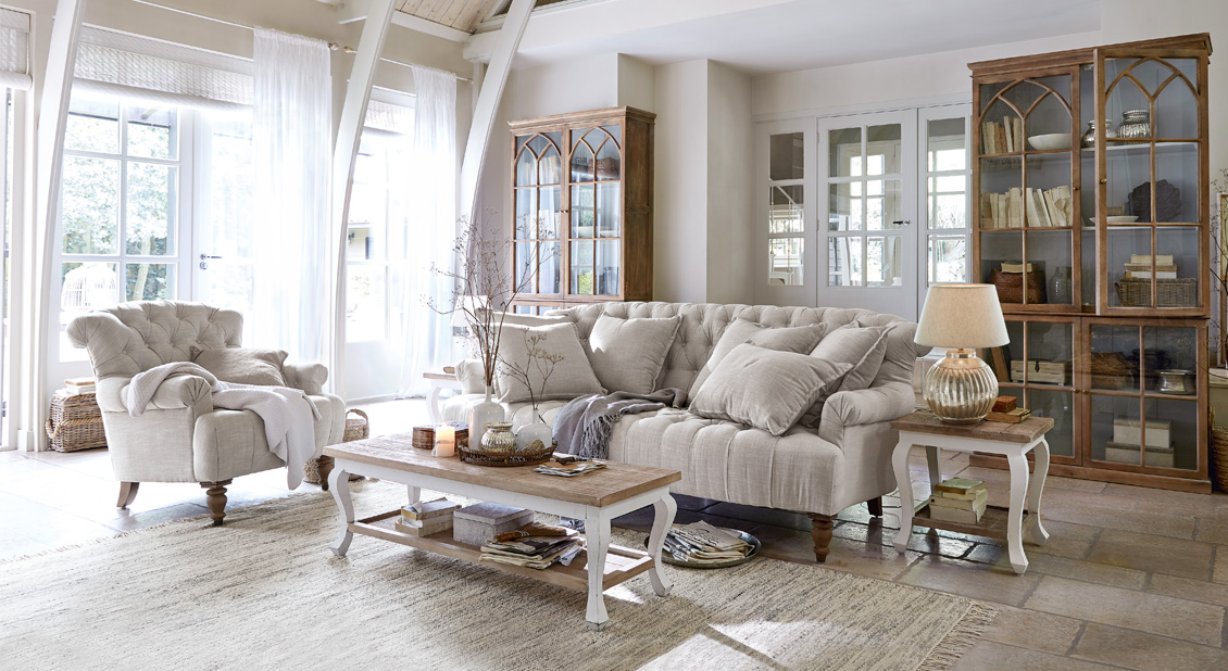 Accogliente soggiorno in stile country con divano e poltrona beige in tessuto, mobili in legno e tappeto chiaro